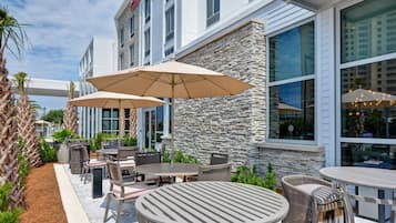 An outdoor patio area with round tables and chairs, large umbrellas, and a stone wall.