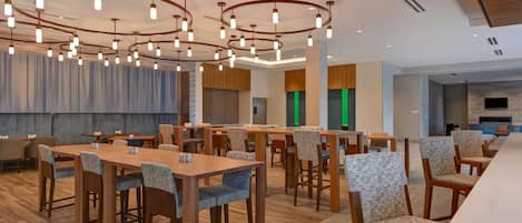 A modern dining area with wooden tables and chairs, a ceiling with circular light fixtures, and a view of a kitchen area in the background.