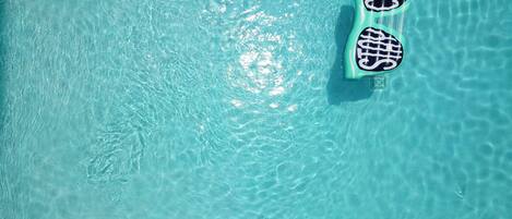 Une piscine d’eau cristalline, avec deux tapis flottants et une échelle.