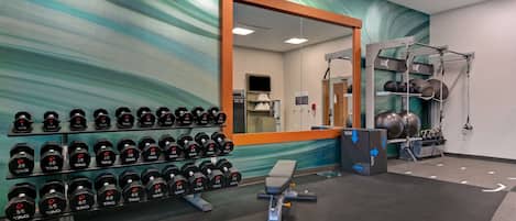 Un gimnasio con racks de pesas, mancuernas, una prensa de banca y pelotas de ejercicio.