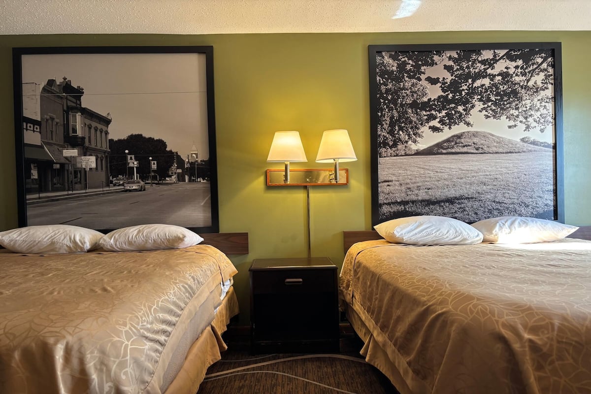 A hotel room with two beds, a nightstand, and two wall-mounted lamps.