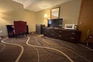 Una habitación de hotel con una tele de pantalla grande, un microondas, una cómoda y una silla.