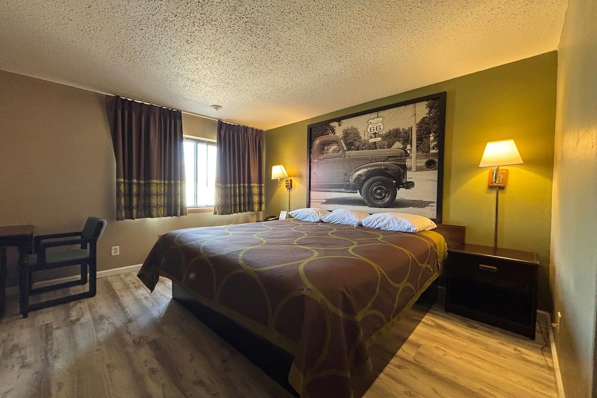 Una habitación de hotel con una cama grande, dos lámparas de noche, un escritorio y una ventana con cortinas.