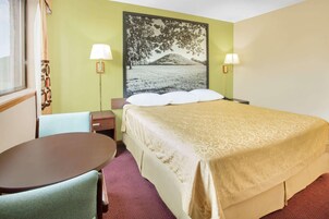 Una habitación de hotel con una cama, dos lámparas de noche, una mesa y una silla.