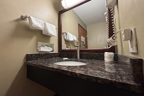 Un baño con encimera de granito, lavamanos, espejo y barra para toallas.