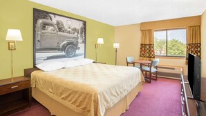 Habitación de hotel con cama, escritorio, silla, televisor y ventana con cortinas.