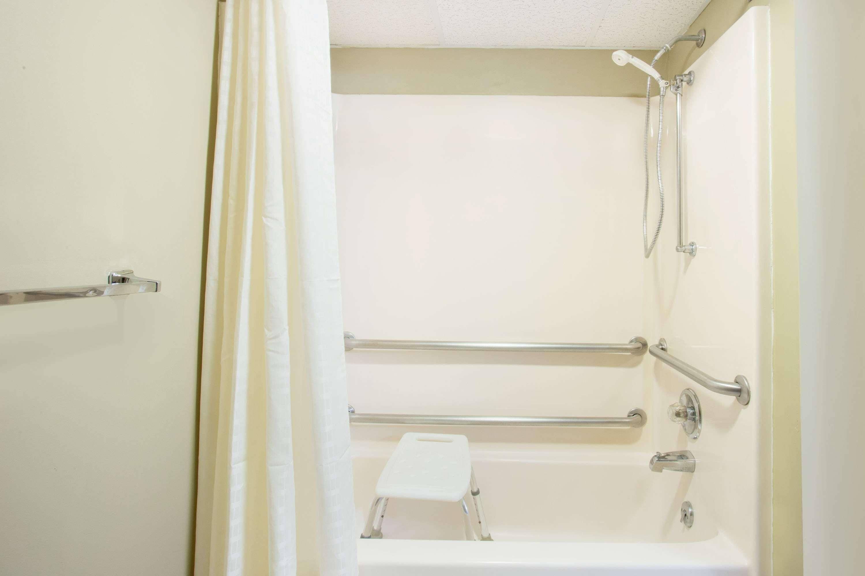 A bathroom with a bathtub, grab bars, a showerhead, and a step stool.