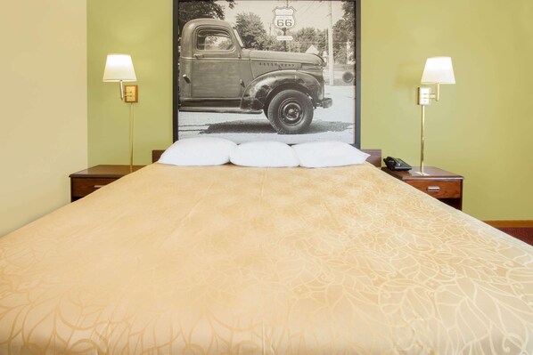 Une chambre d’hôtel avec un lit, deux lampes de chevet, un téléphone et une affiche représentant un camion d’époque accrochée au mur.