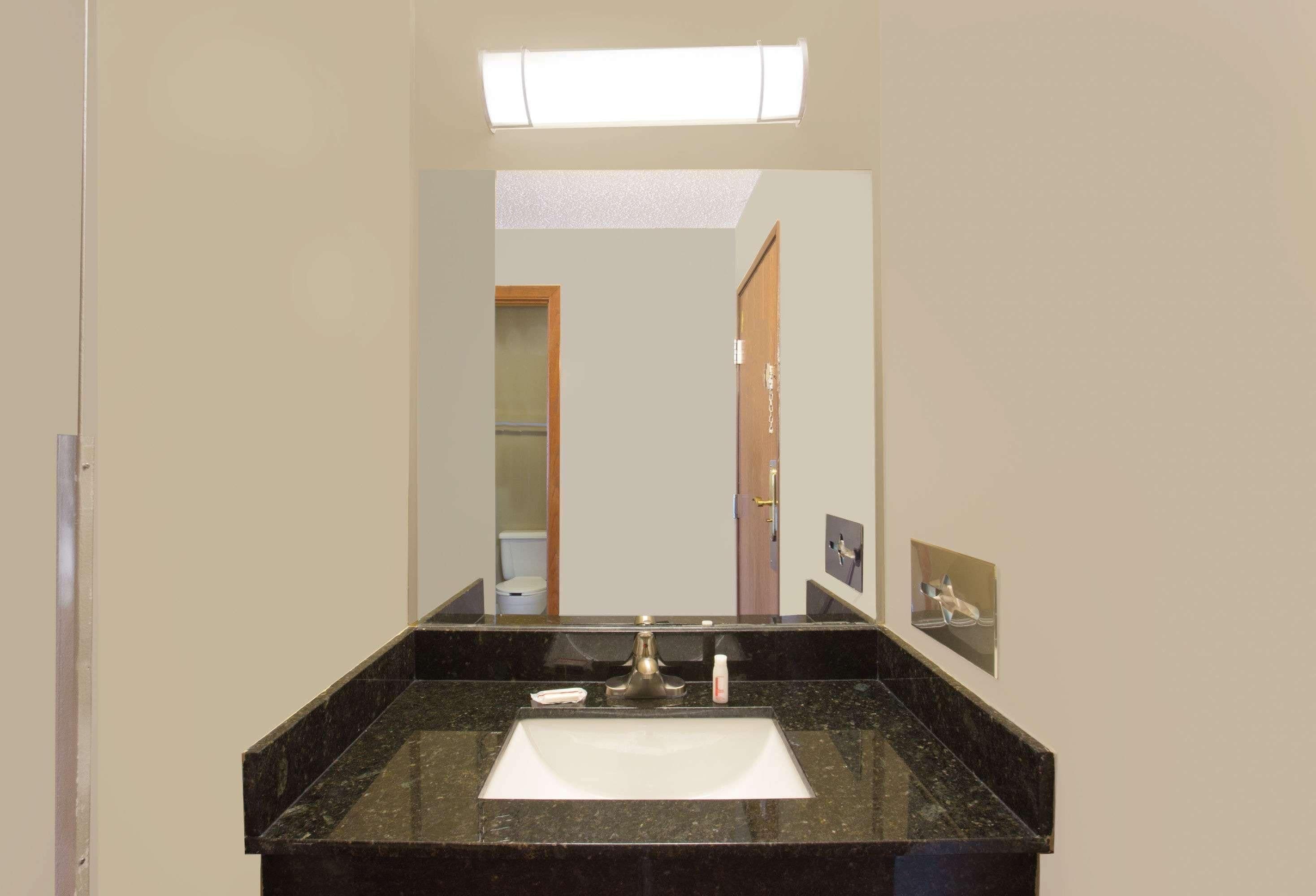 A bathroom with a black marble sink, a mirror, a light fixture above the mirror, and a door leading to another room.