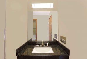 Un baño con lavamanos de mármol negro, un espejo, una lámpara sobre el espejo y una puerta que da a otra habitación.