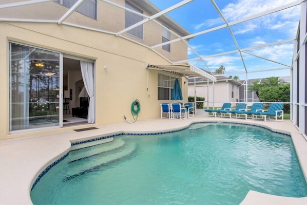 A swimming pool with blue chairs, a covered patio, and a glass door leading to a room.