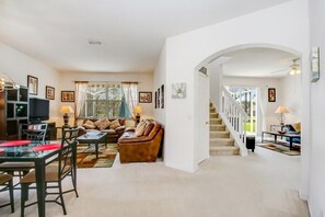 A spacious living room with a sofa, coffee table, and TV, a dining area with chairs and a table, and a staircase leading to another level.