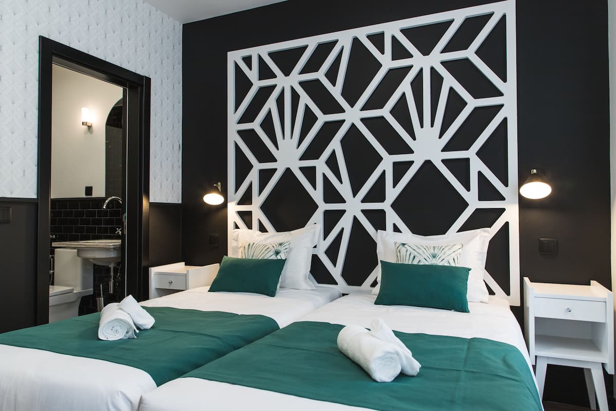 Een hotelkamer met twee bedden, een grote spiegel, een wit hoofdeinde en een nachtkastje.