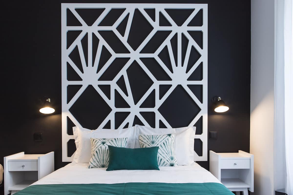 Een moderne hotelkamer met een hoofdbord met een geometrisch patroon, een opgemaakt bed met wit en teal beddengoed en twee nachtkastjes met lampen.
