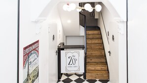 Un escalier avec un sol à carreaux noirs et blancs, une rampe en bois et une pancarte indiquant « chambres et suites de style années 20 ».