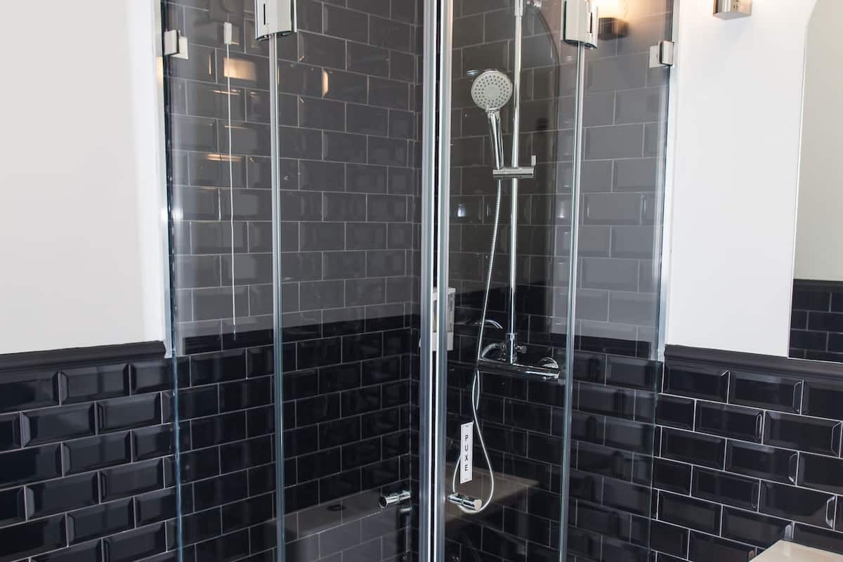 Een moderne badkamer met een douchecabine van glas, zwart betegelde wanden, een wit toilet en een wastafel.