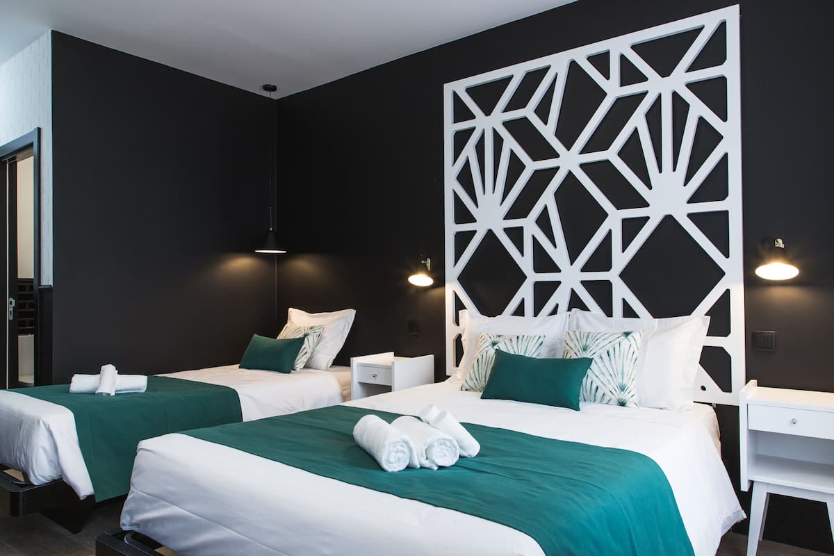 Een hotelkamer met twee bedden, elk voorzien van groen-wit beddengoed, een wit hoofdeinde en een geometrisch wandpaneel.
