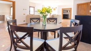 A dining area with a round table and six chairs, a vase with flowers, and a kitchen in the background. - Villa Near Ibiza Town Sleeps 12/14 (Cap Martinet)