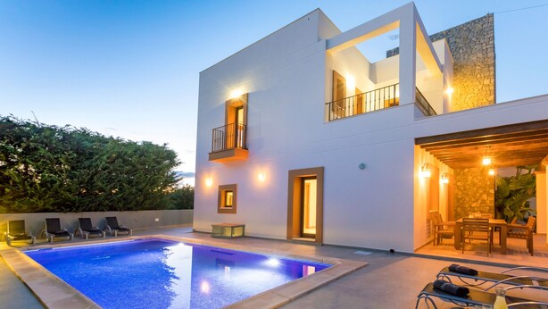 A modern two-story house with a swimming pool, outdoor seating, and a stone wall. - Villa Near Ibiza Town Sleeps 12/14 (Cap Martinet)