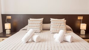 A neatly made bed with two pillows, two rolled towels, and two bedside lamps on wooden nightstands. - Villa Near Ibiza Town Sleeps 12/14 (Cap Martinet)