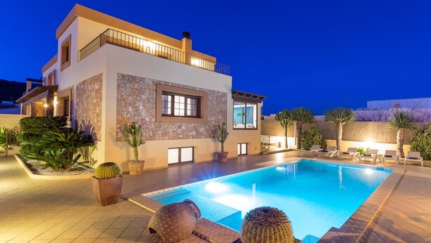 Une maison moderne à deux étages, dotée d’une piscine, d’une façade en pierre et d’un espace extérieur aménagé pour se détendre.