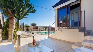 Un espace aménagé au bord de la piscine, avec une table en verre, des chaises longues et un escalier menant à un balcon.