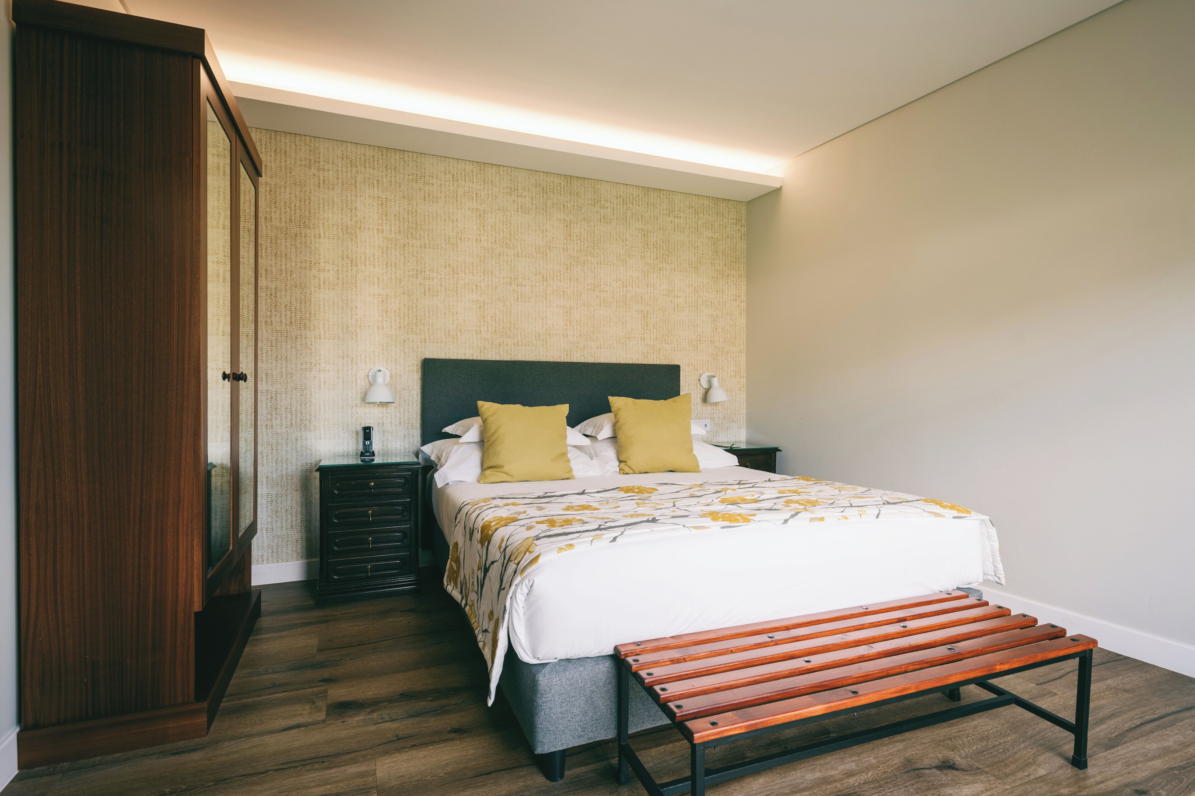 A bedroom with a bed, bedside tables, a bench, and a wardrobe.