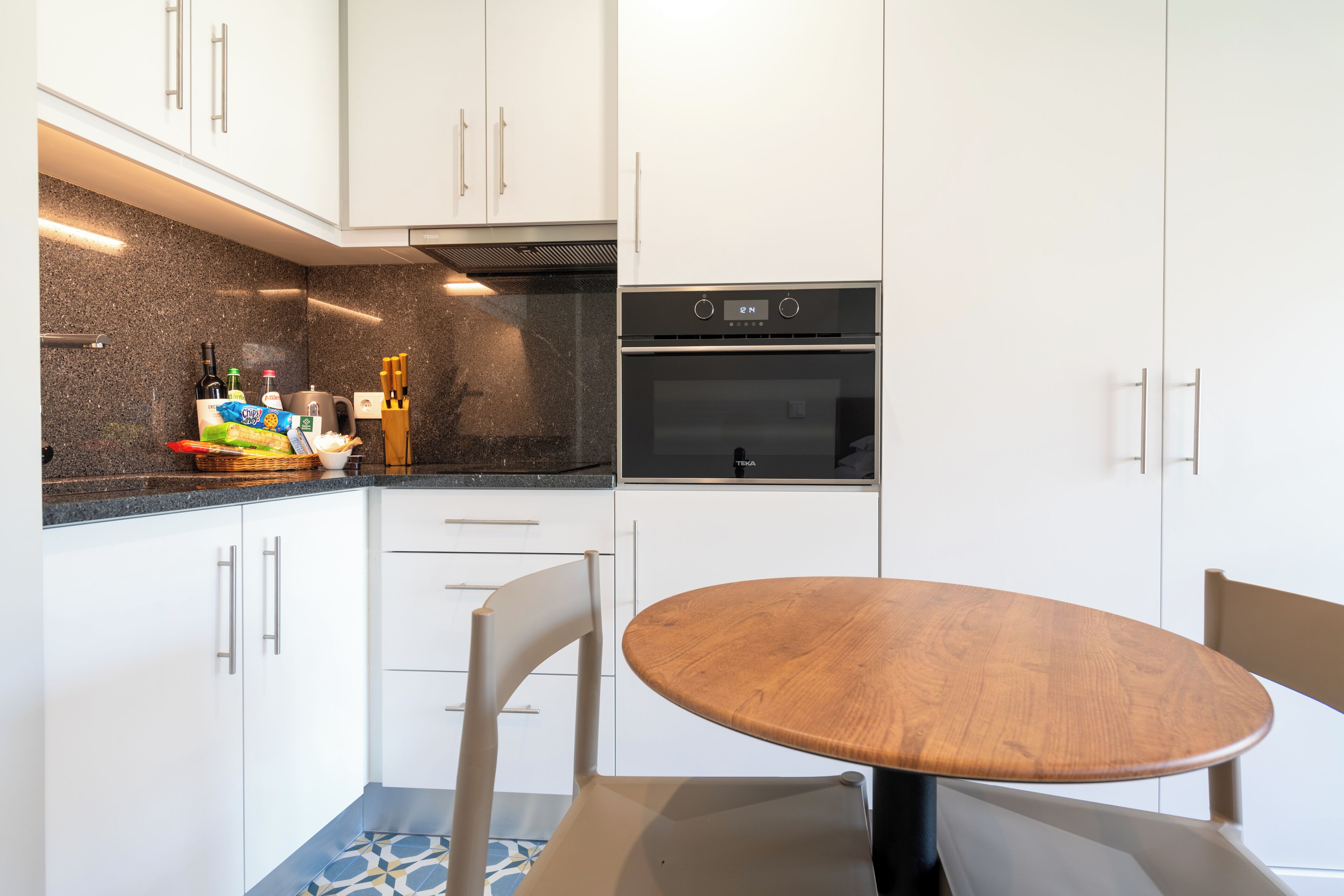 A modern kitchen with white cabinets, a black oven, and a wooden dining table.