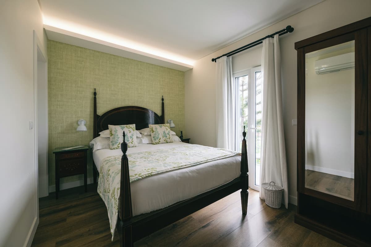 A neatly arranged bedroom with a wooden bed, a bedside table, a lamp, and a window with curtains.