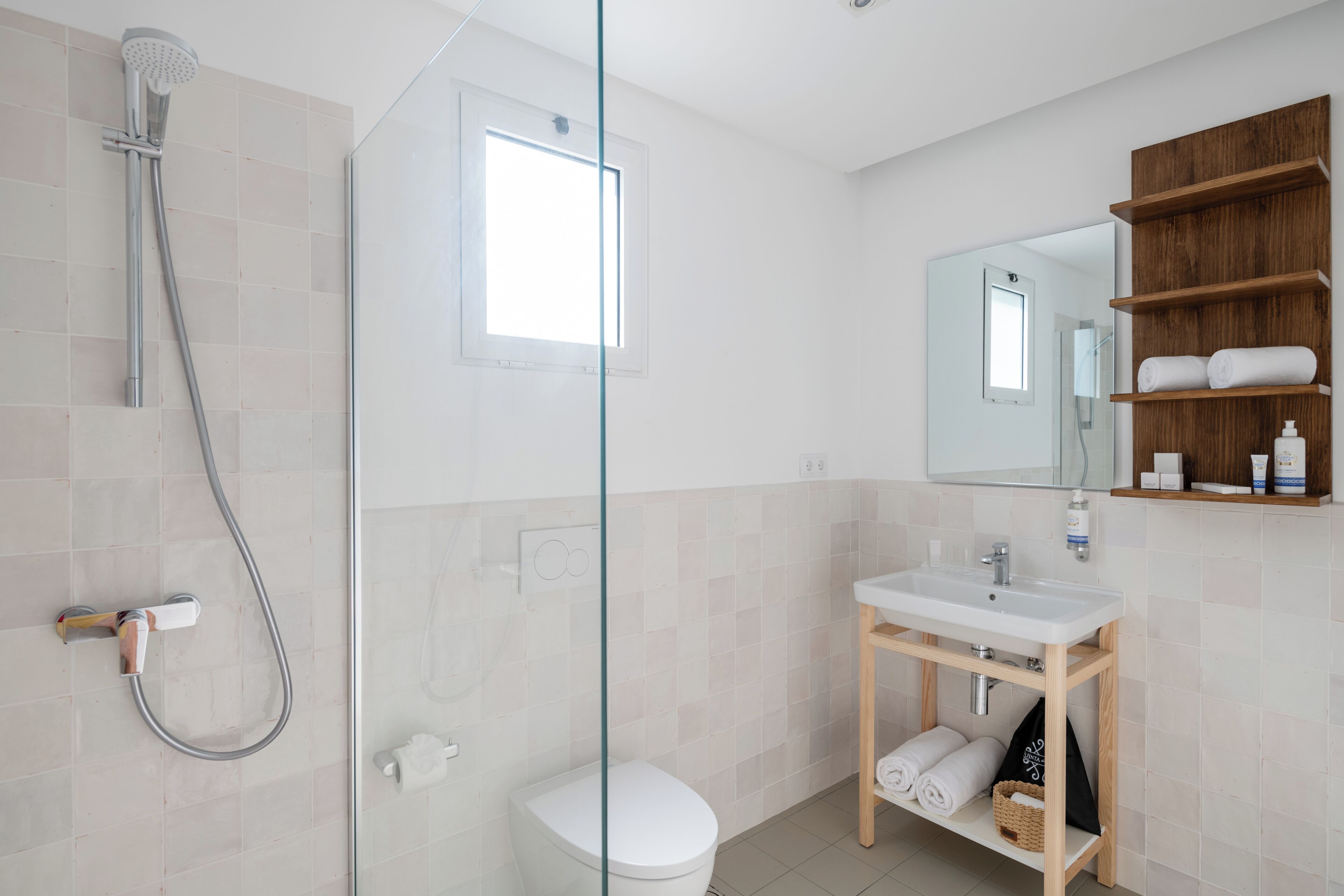 Ein modernes Badezimmer mit Duschkabine aus Glas, Toilette in Weiß und einem Holzwaschtisch mit Spiegel und Ablageflächen.