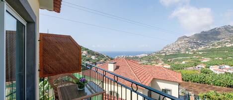A balcony with wicker furniture, a view of a coastal town, and a tiled floor.