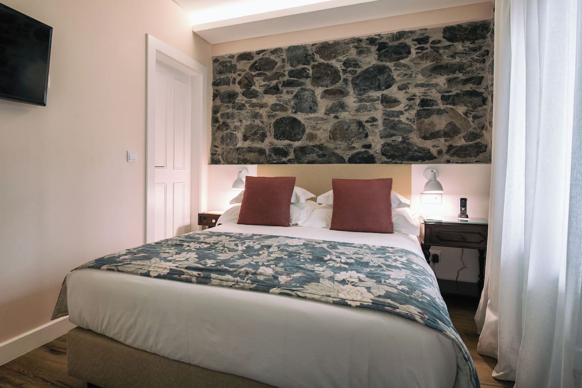 A bedroom with a stone wall, a bed with floral bedding, two bedside lamps, and a nightstand.