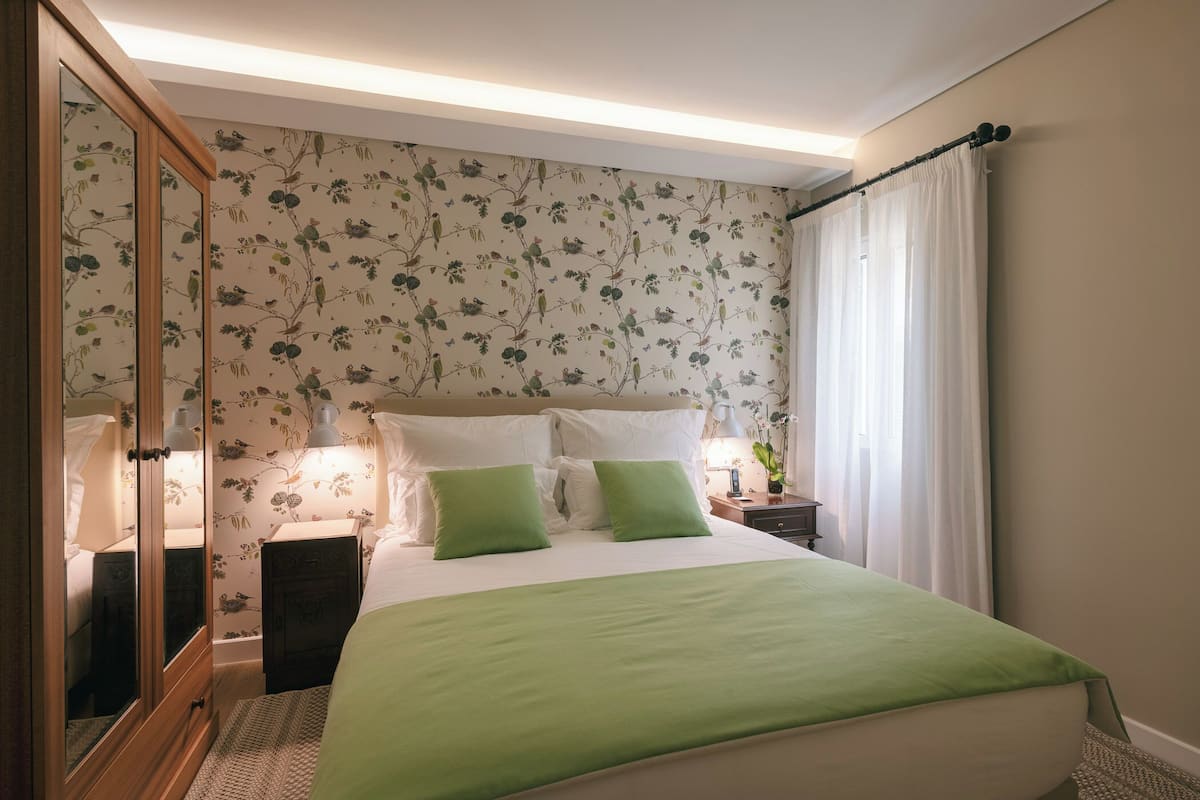 A bedroom with a bed, green pillows, a nightstand, a lamp, and a mirror.