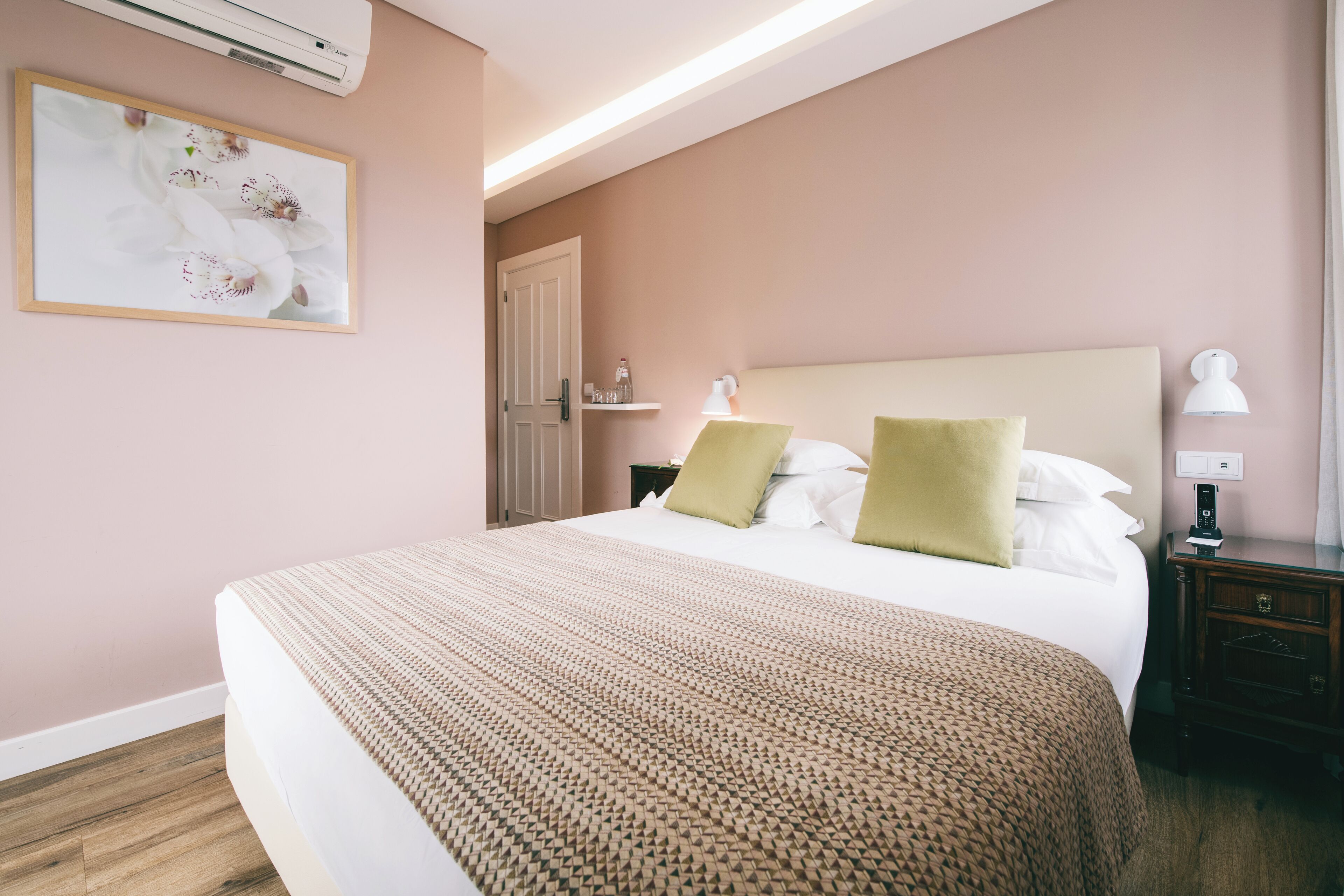 A neatly made bed with a patterned bedspread, a bedside lamp, and a framed floral artwork on the wall.