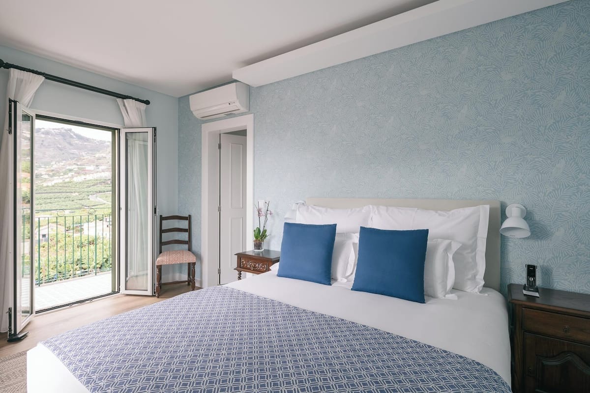 A bedroom with a large bed, a chair, a nightstand, and a view of a balcony.