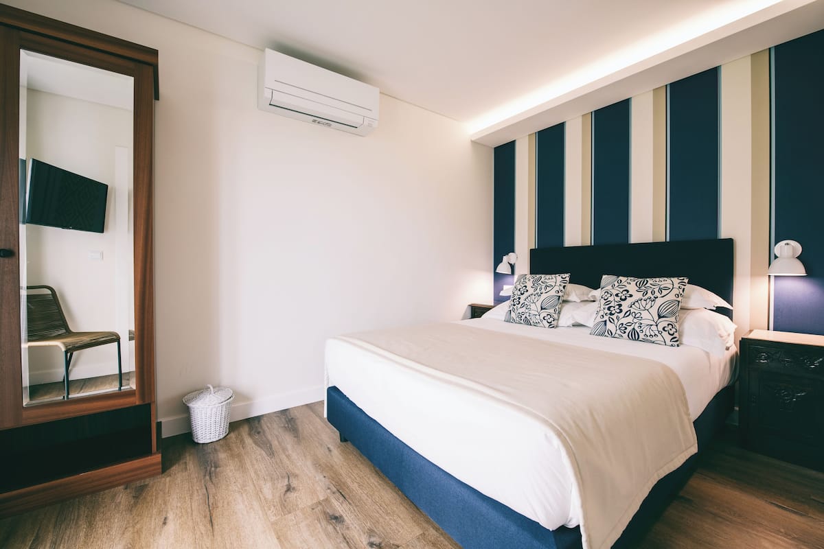 A bedroom with a bed, bedside tables, a TV mounted on a wall, and an air conditioning unit.