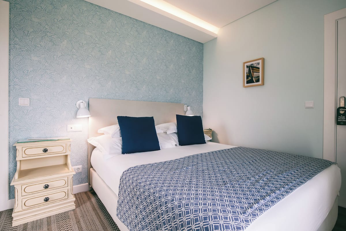 A hotel room with a bed, a nightstand, a lamp, and a framed picture on the wall.