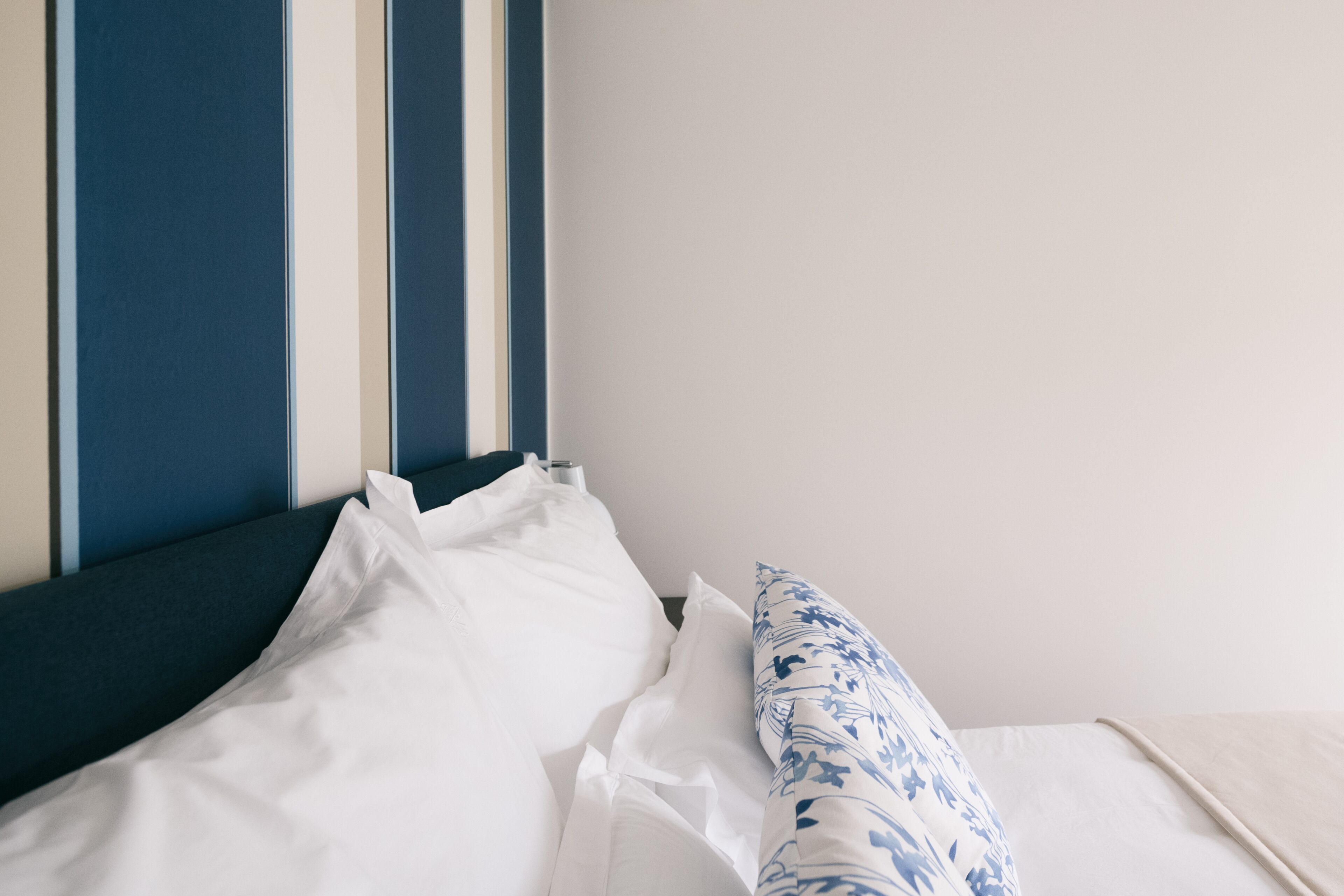 Ein ordentlich bezogenes Bett mit weißer und blauer Bettwäsche, einem gestreiften Kopfteil und einer schlichten Wand.