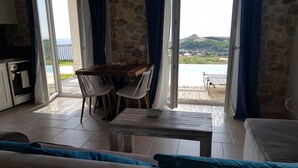 Ein Zimmer mit Steinwand, einem Holztisch mit Stühlen, einer Couch und Blick auf eine bergige Landschaft durch große Fenster.