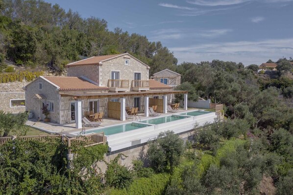 A stone villa with a swimming pool, outdoor seating, and a view of the surrounding forest.