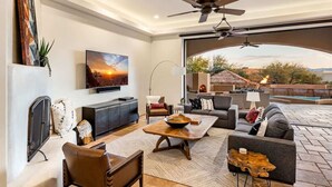 Un salón amplio con chimenea, televisor y un ventanal con vistas a una zona de piscina.