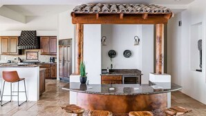 Una cocina con una isla central, taburetes de madera, una planta en maceta y un techo de baldosas.