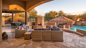 Un patio techado al aire libre con piscina, mobiliario de mimbre y una chimenea.
