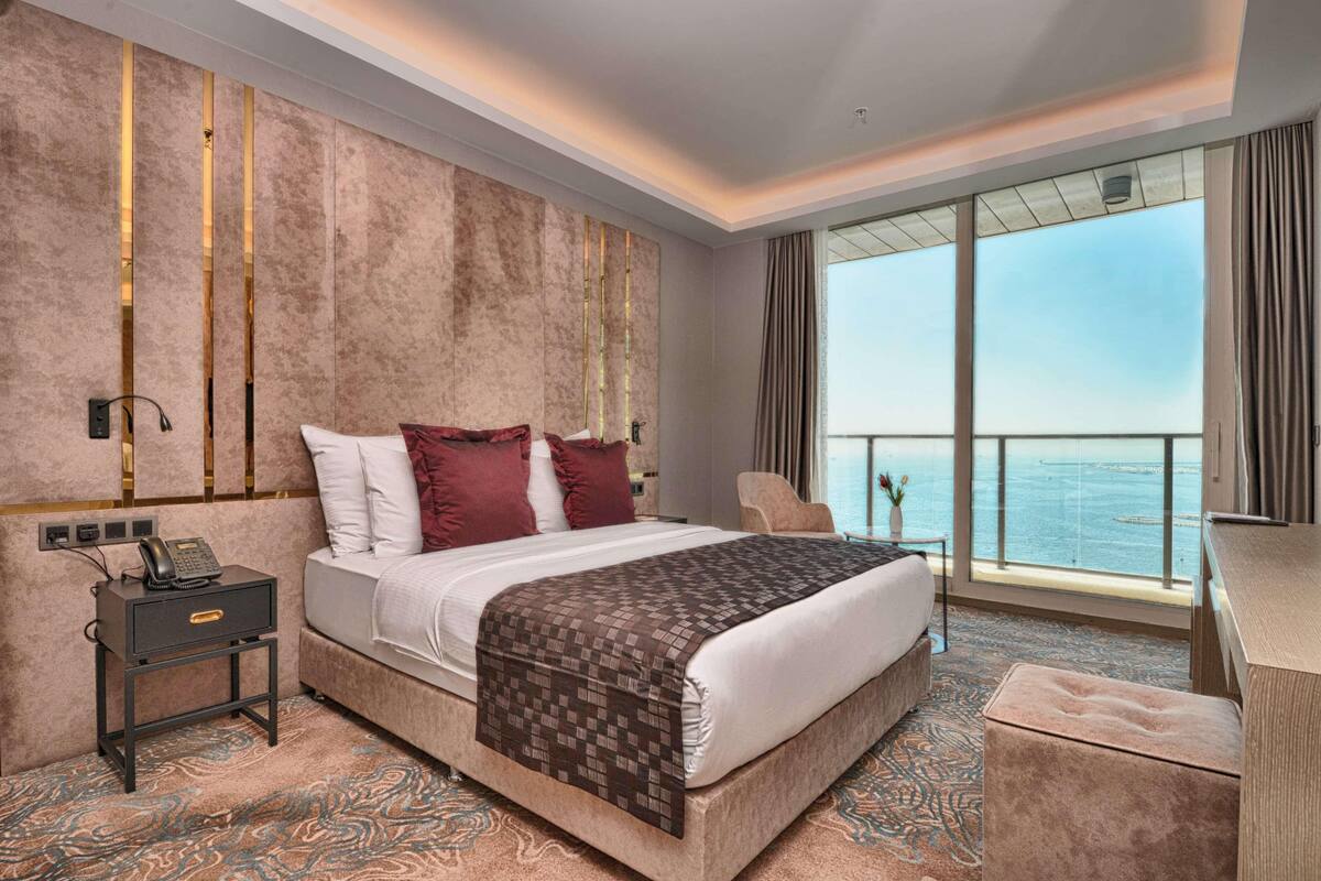Habitación de hotel con una cama grande, una mesita de noche con teléfono, una silla, un escritorio y vistas al mar.