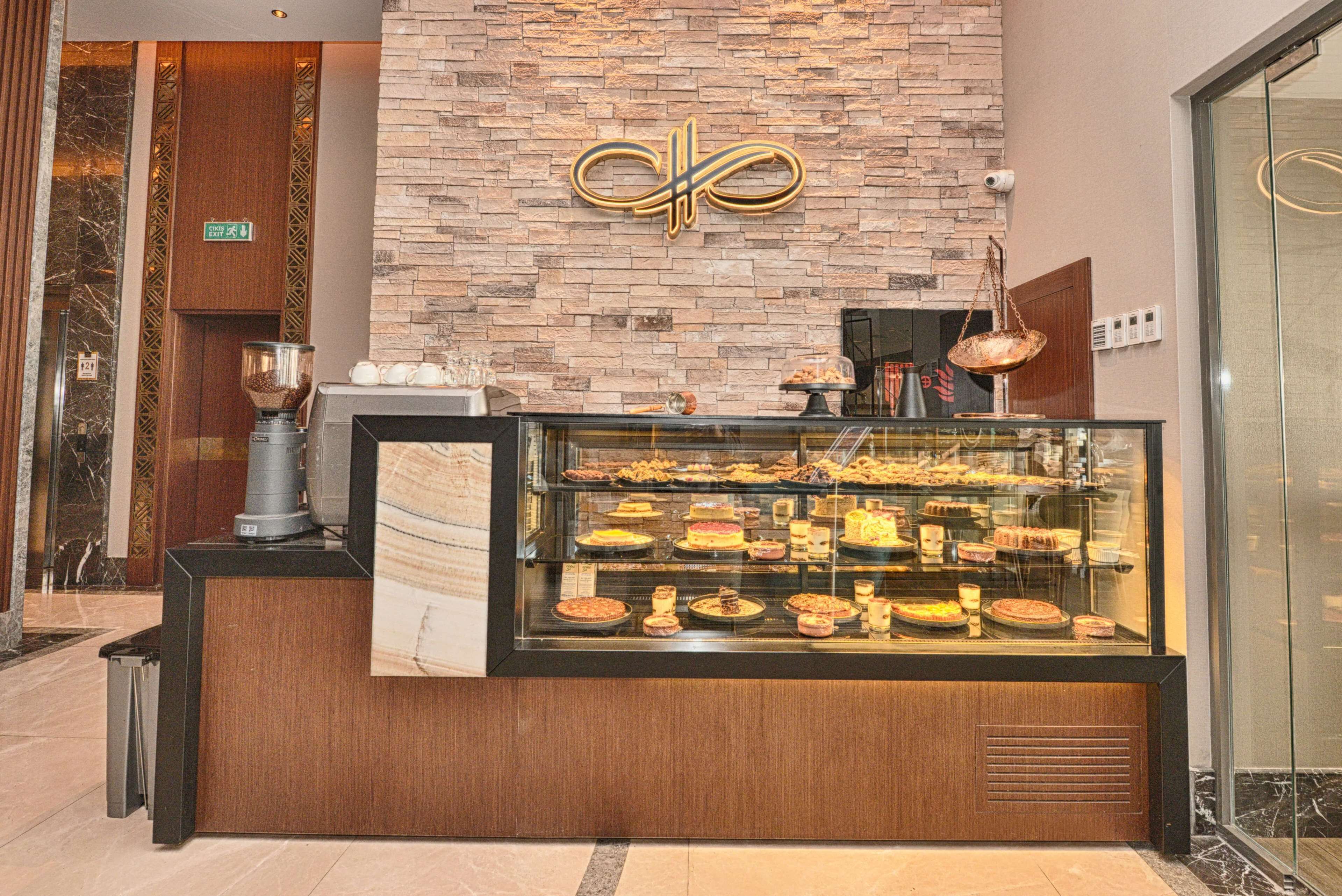 Vitrine de pastelaria com diversos produtos de pastelaria, uma máquina de café e uma parede decorativa com um logotipo.