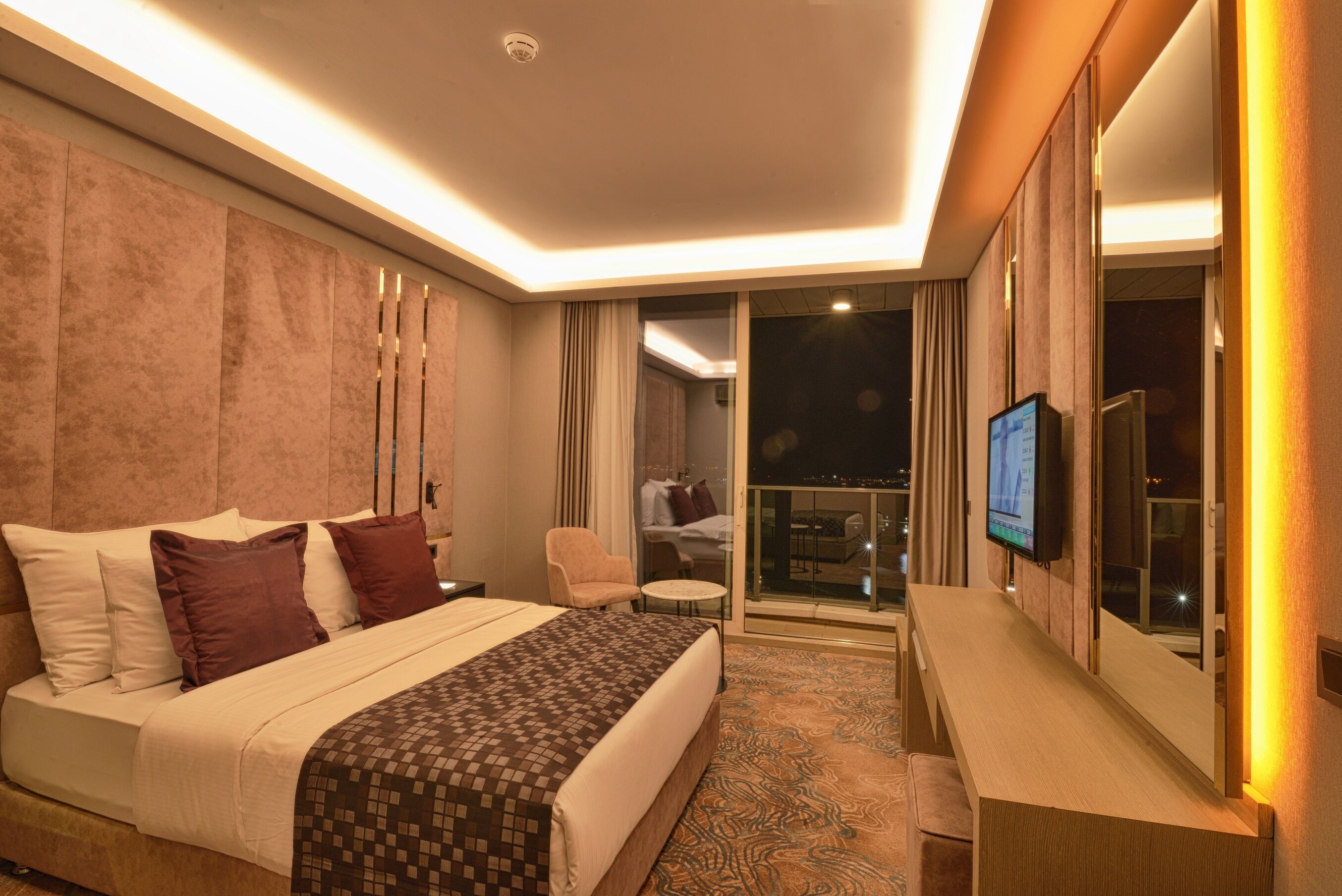 Une chambre d’hôtel moderne dotée d’un grand lit, d’une télévision, d’un balcon avec vue et d’un bureau.