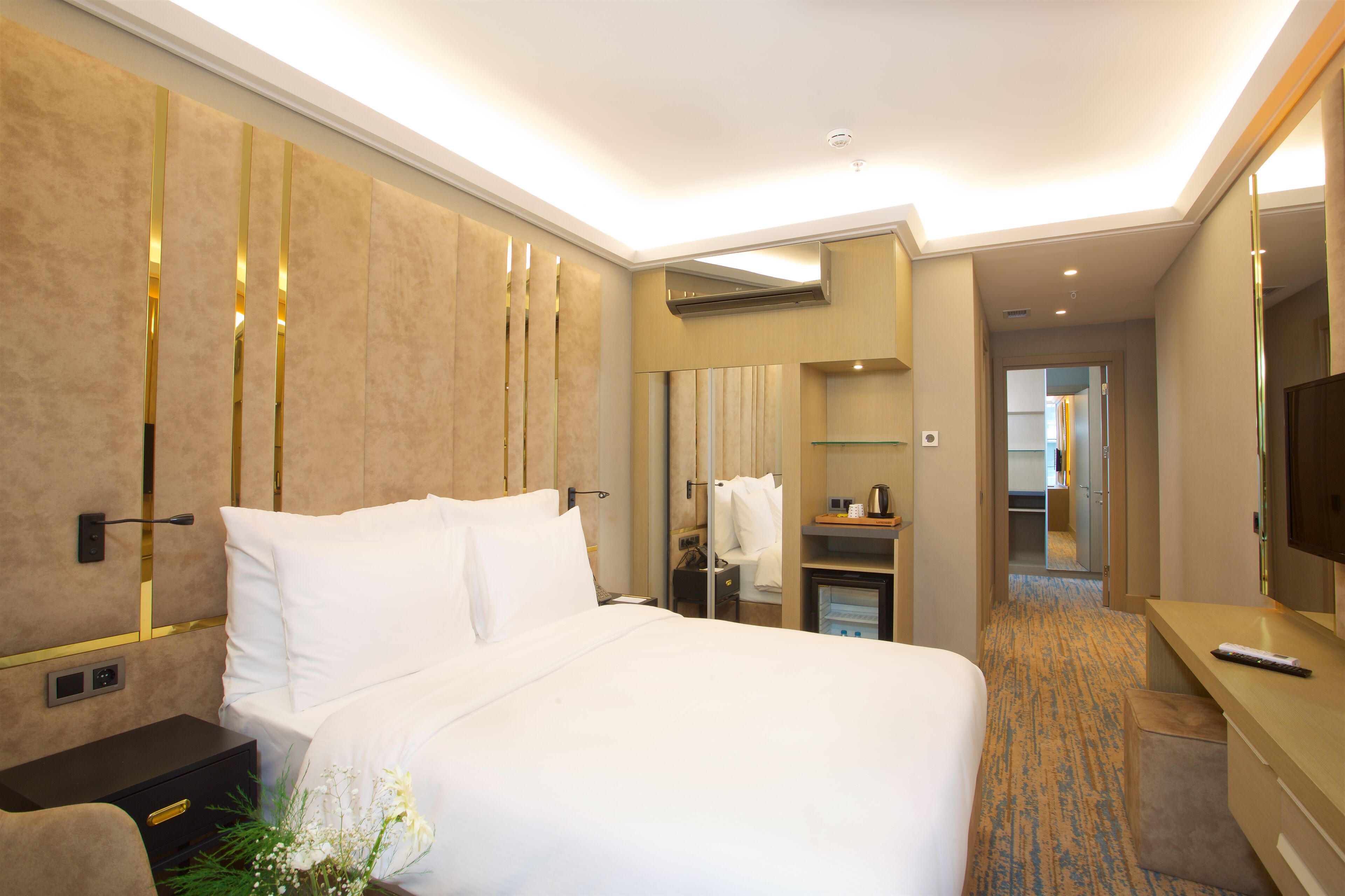 A hotel room with a large bed, bedside tables, a mirror, a TV, and a bathroom visible through an open door.