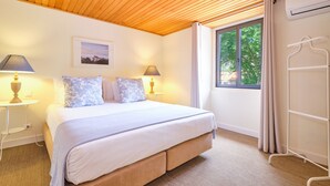 A bedroom with a wooden ceiling, a bed with a white and blue floral bedspread, two bedside lamps, a framed picture on the wall, and a window with curtains. - Sintra Bliss A Part (Sintra)