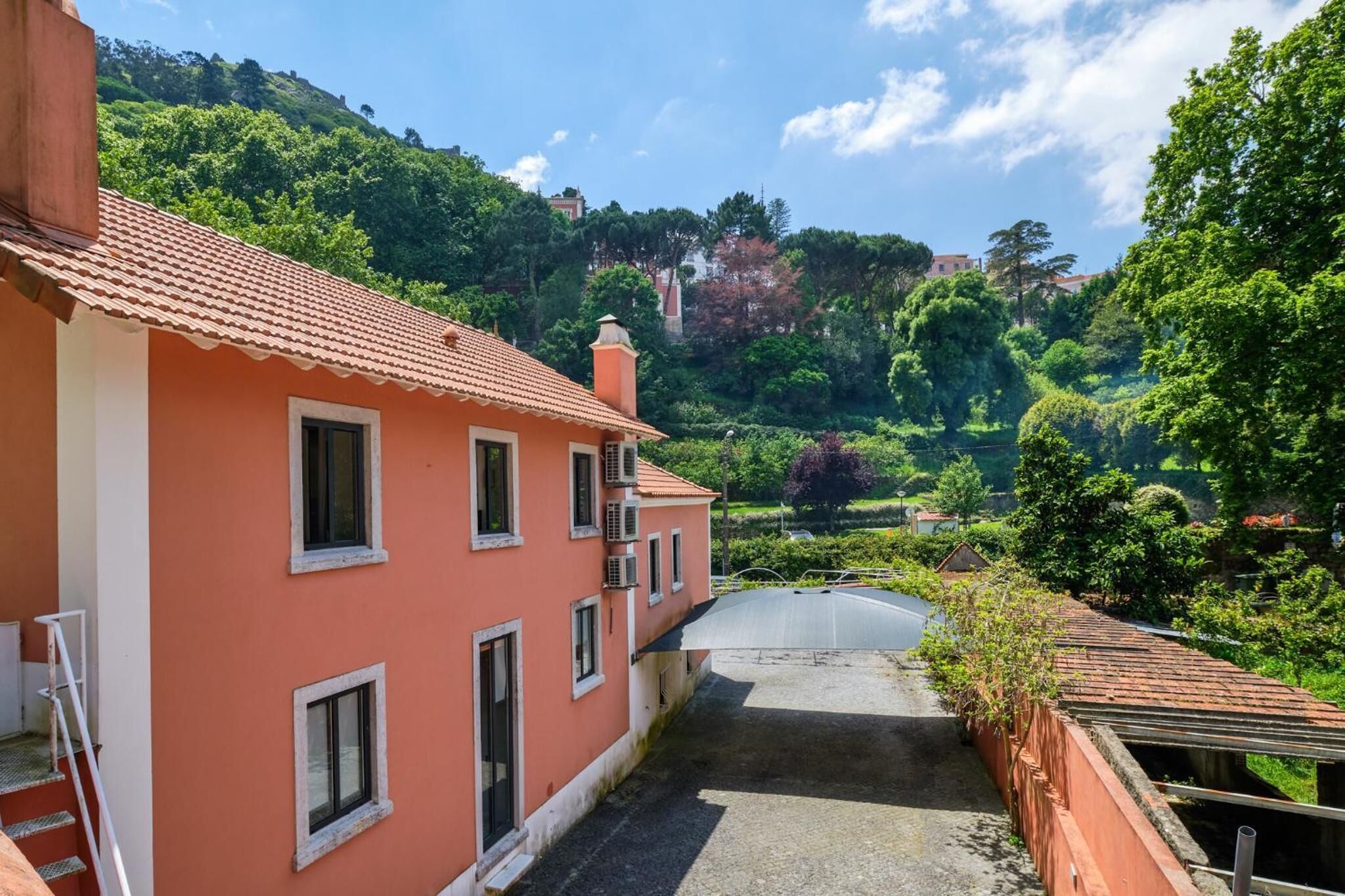 Ein Gebäude mit roter Fassade, einem kleinen Balkon und Blick auf einen üppigen, grünen Hügelhang.