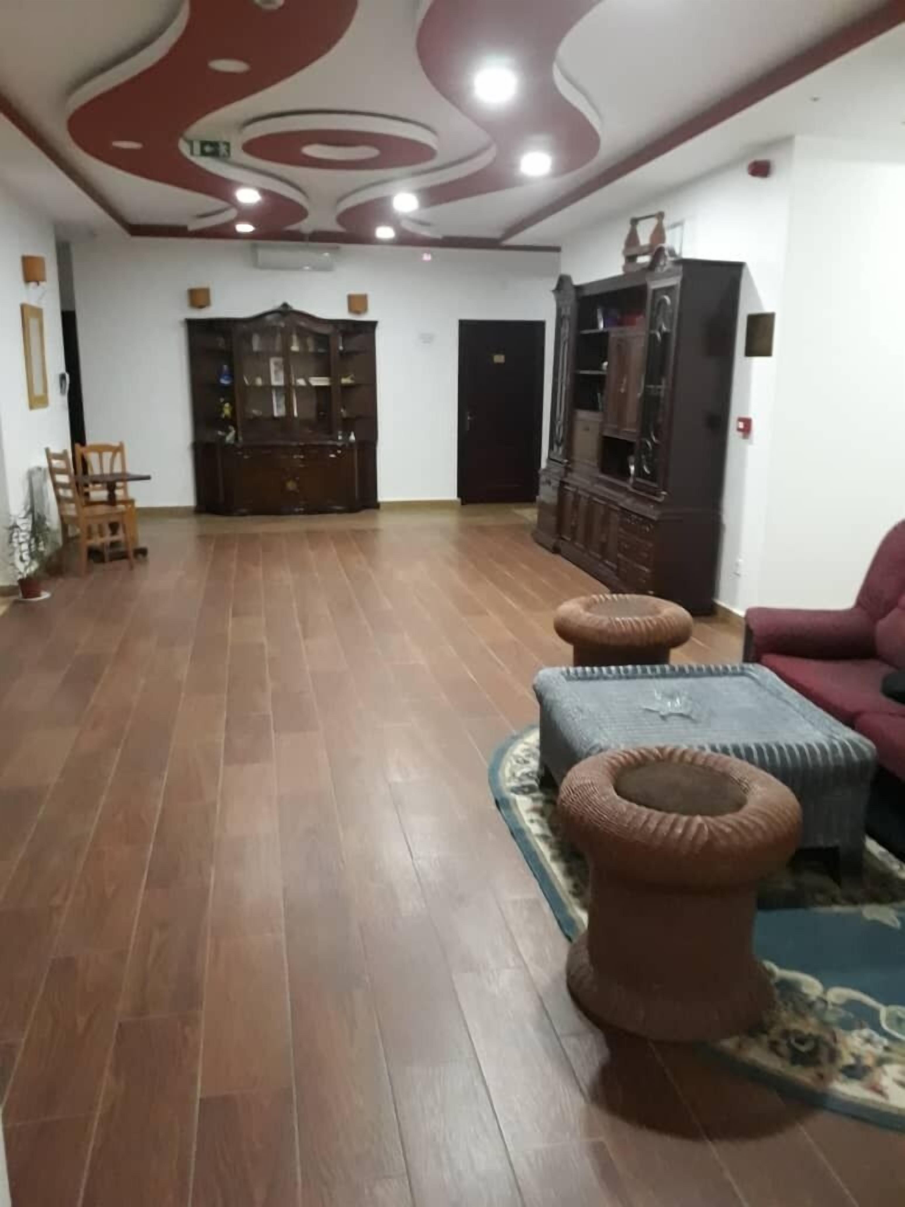 Una habitación amplia con suelo de madera, un mueble grande de madera y una zona de estar con otomanas y una silla.